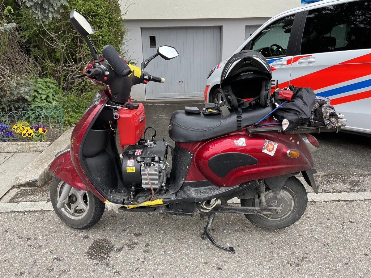 Ein roter E-Roller mit einem Benzingenerator auf dem Trittbrett.